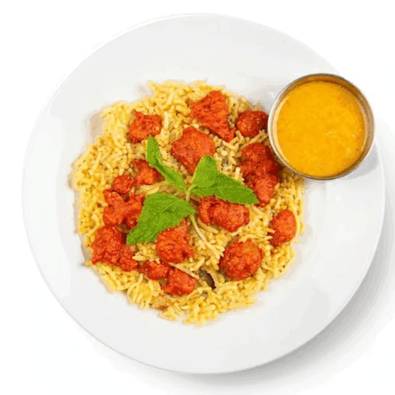 Chicken tikka biryani with rice, red chicken pieces, mint garnish, and a side of yellow sauce.