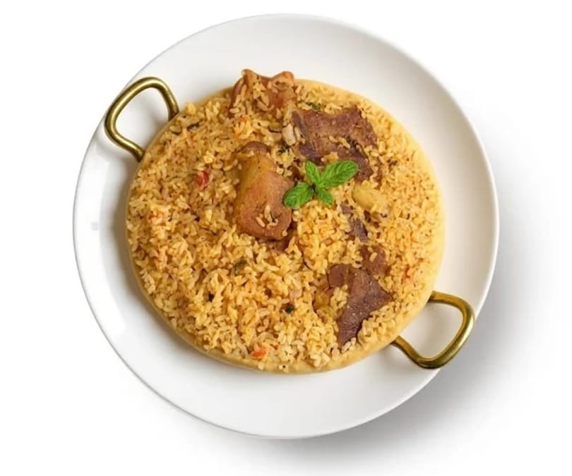 A round, golden biryani dish with meat and a mint garnish, served on a white plate.