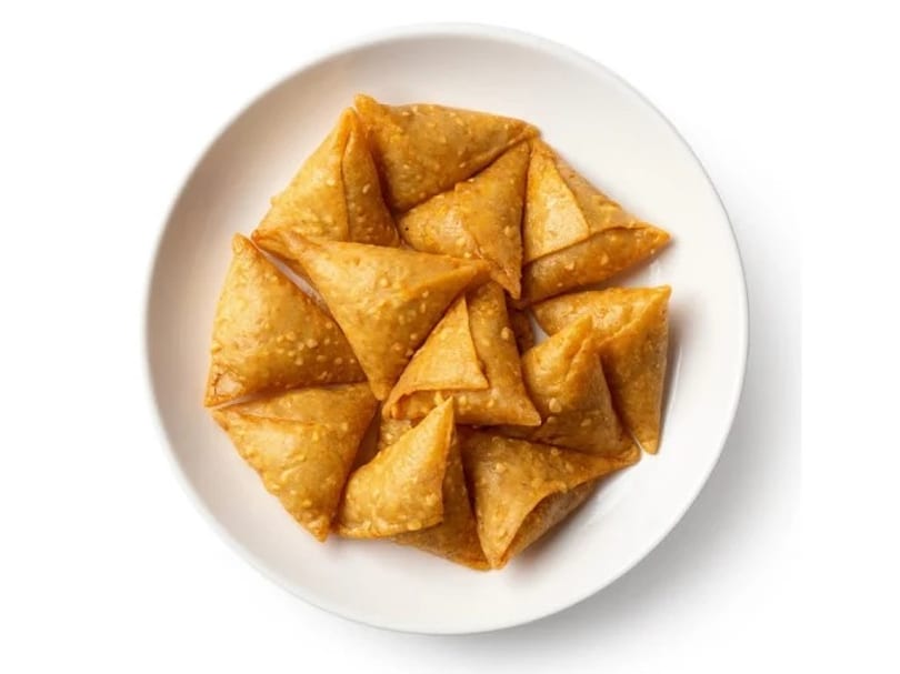 A white plate filled with golden-brown, triangular mini samosas, sprinkled with sesame seeds.