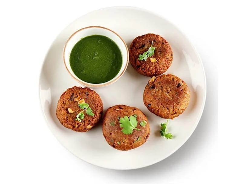 Four golden-brown lentil fritters with cilantro garnish, served with a bowl of green chutney.