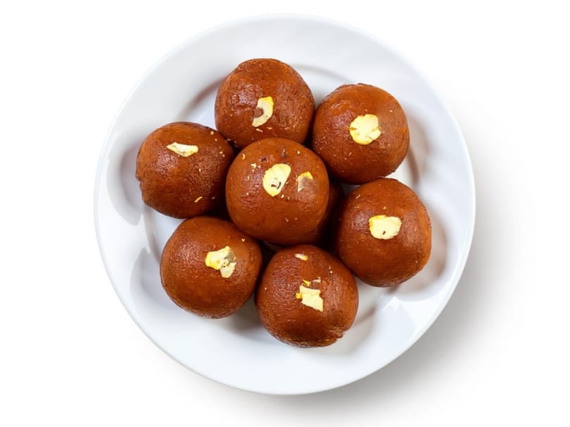 Seven brown gulab jamun, garnished with slivered almonds, arranged on a white plate.