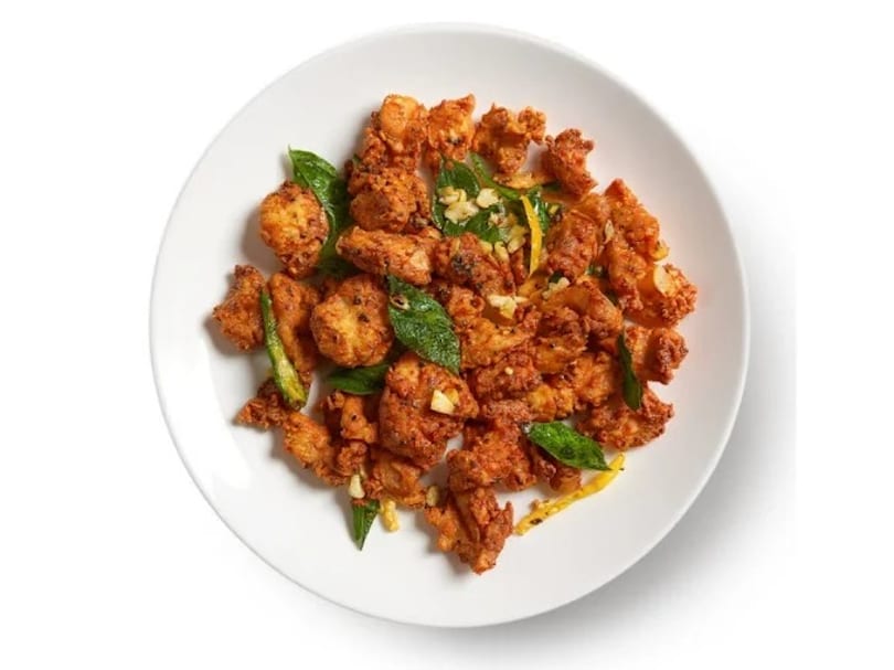 Crispy fried chicken pieces with green herbs and yellow strips on a white plate.