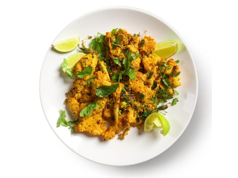 Spicy chicken tikka, garnished with fresh cilantro and lime wedges, on a white plate.